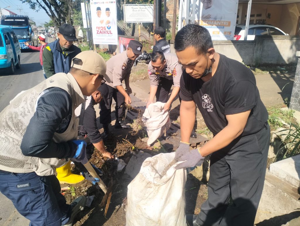 Anggota Polsek Sukalarang Bantu Warga Lakukan Kerja Bakti Bersihkan Selokan dan Rerumputan Liar di Jalan Protokol Nasional